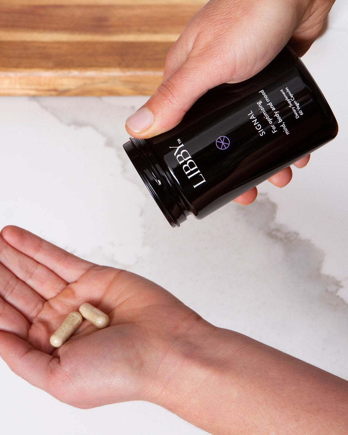 Signal supplement from Libby being poured from black bottle into palm of hand.