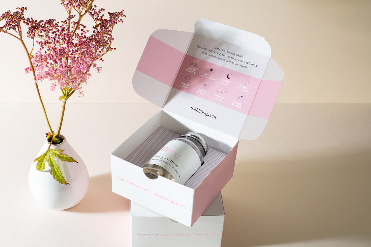 Bottle of libby in its packaging next to a pink flower in a white vase